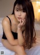 A woman in a black lingerie sitting on a bed.