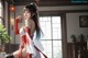 A woman in a red and white outfit with long hair stands indoors near a window.