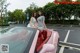 Two women sitting in the back of a pink convertible car.