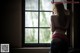 A woman standing in front of a window looking out the window.